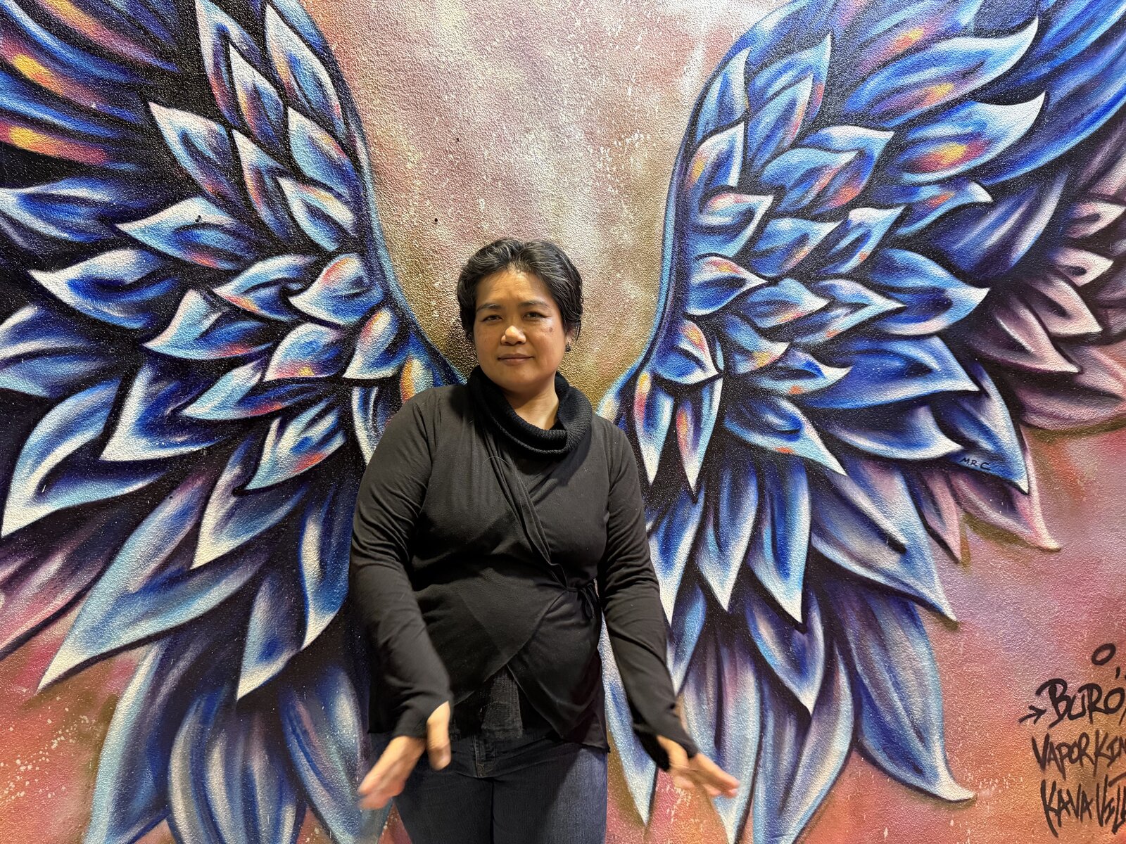 Lasaly Changkachith standing in front of a winged mural
